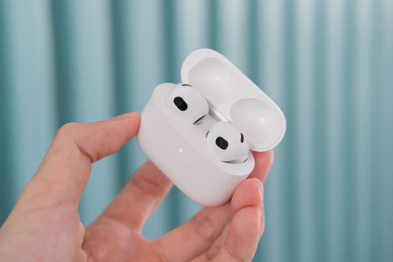 AirPods 3 met open oplaadcassette in de hand op blauwe achtergrond