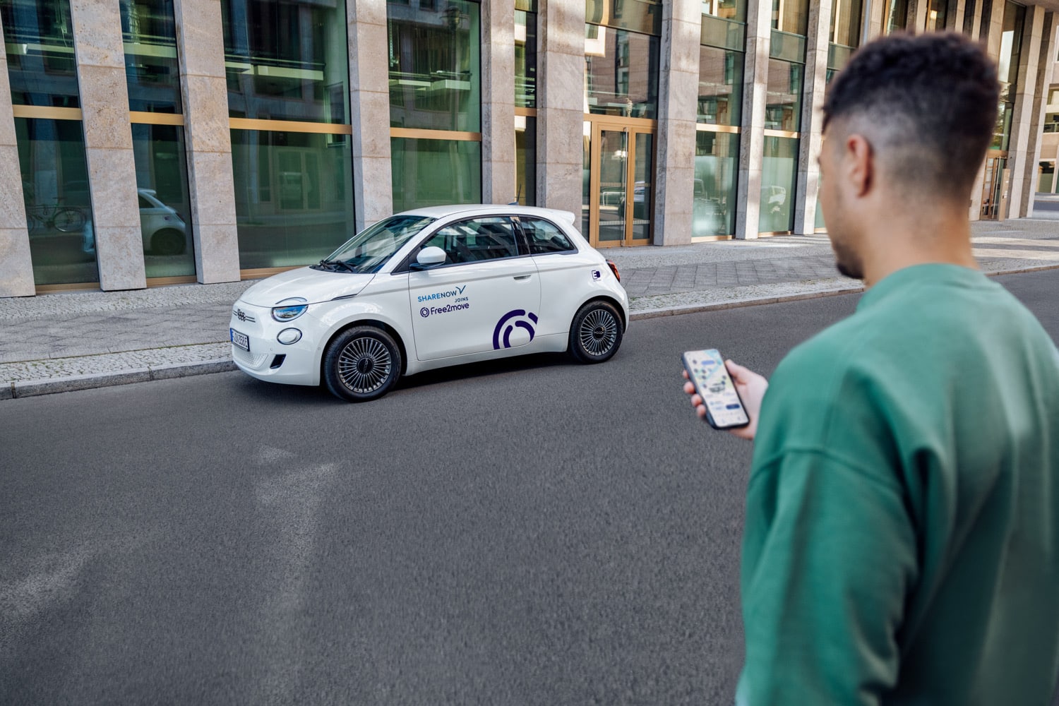Eine Person mit Share Now-App bewegt sich auf ein weißes Share Now-Auto zu
