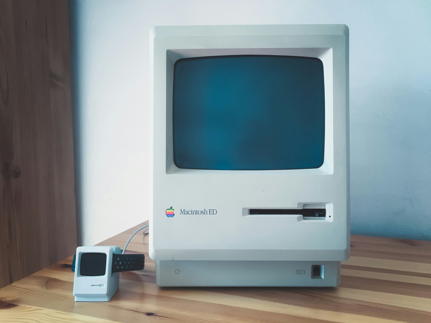 Apple Macintosh aus 1984 auf einem Schreibtisch, daneben ein Mini-Macintosh als Apple Watch-Ladestation