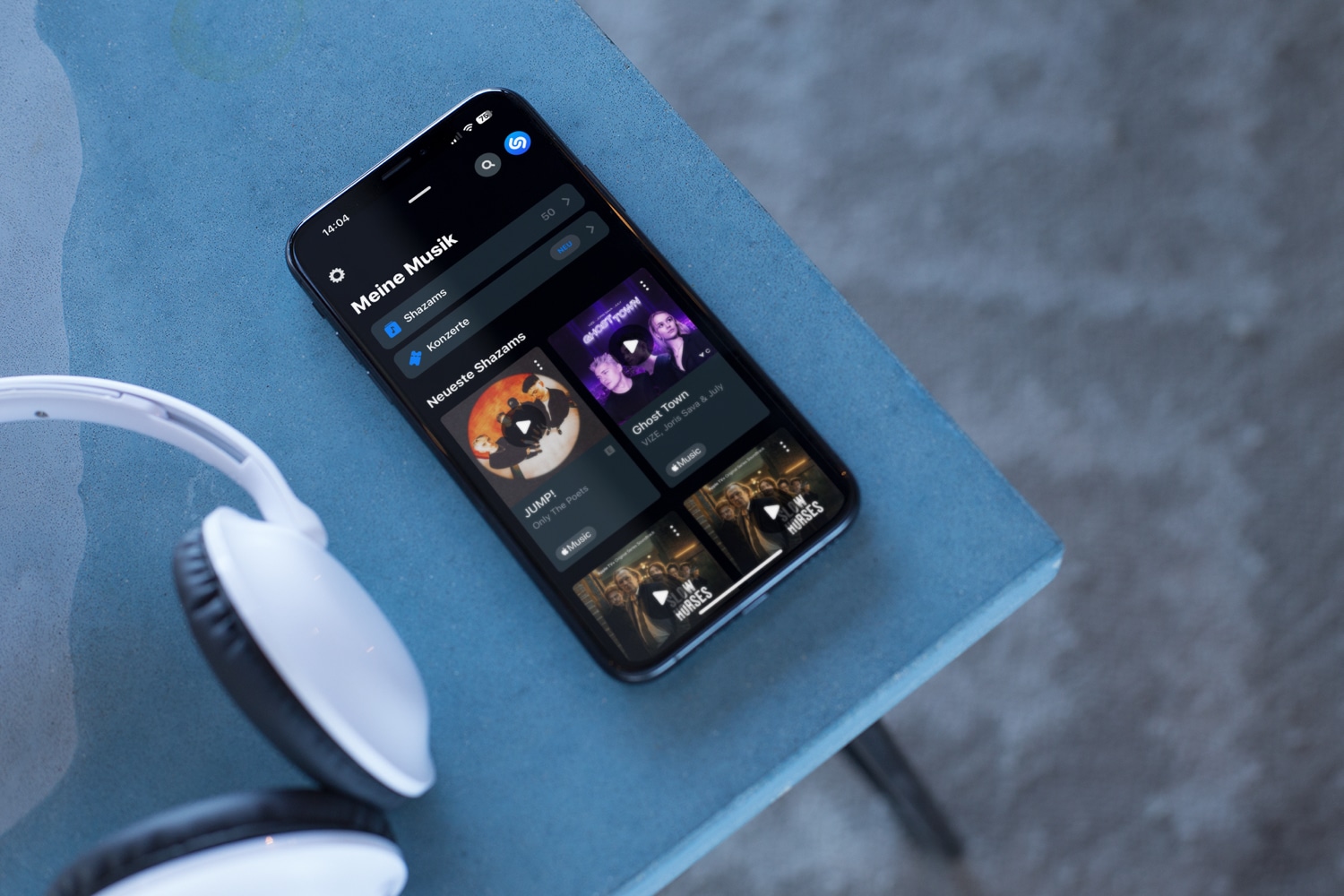 iPhone-Mockup von Shazam mit Kopfhörer auf einem blauen Tisch