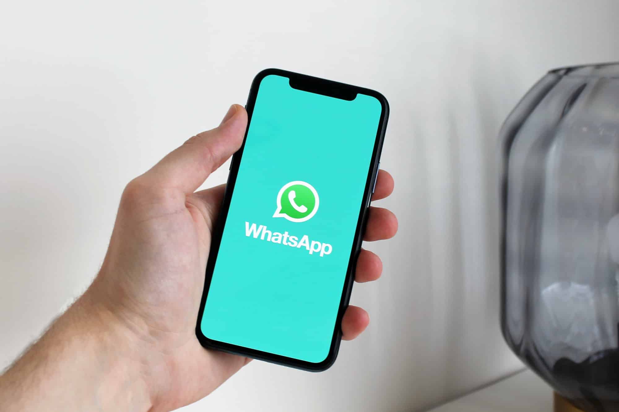 Eine Person hält ein iPhone in der Hand, auf dem ein grüner Bildschirm mit dem WhatsApp-Logo zu sehen ist