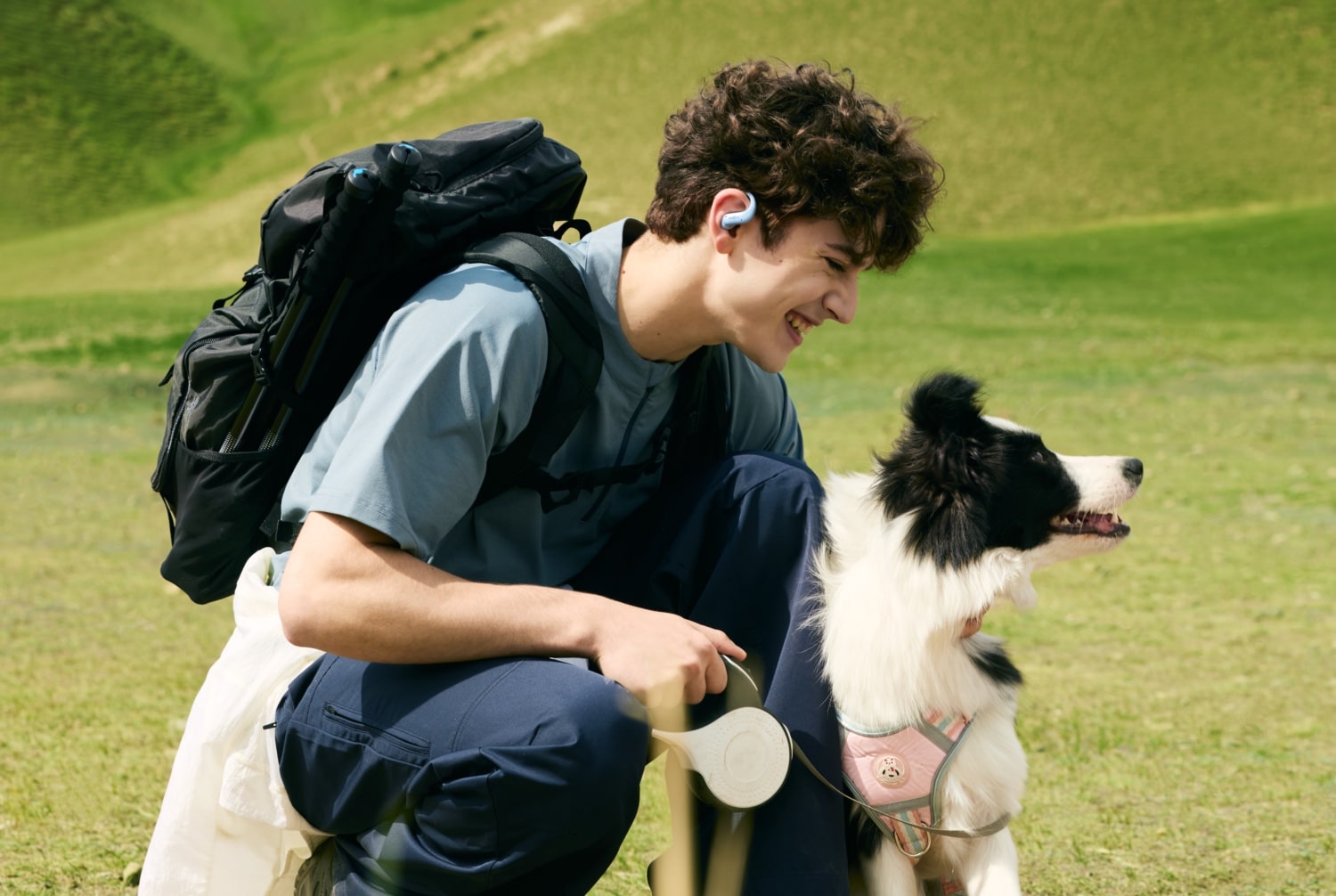 Eine Person mit einem Bordercollie wandert in der Natur und trägt die Shokz OpenFit Air 2 in Blau